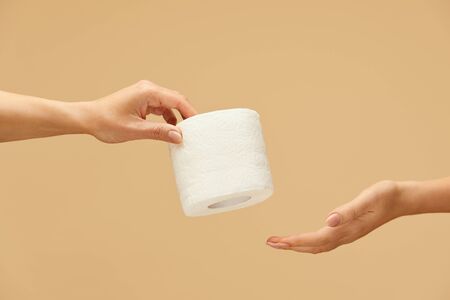 Hygiene. Toilet Paper Roll In Female Hand On Beige Background. One Woman Gives Tissue Paper To Another. Using High-Quality Product For Staying Healthy During Coronavirus Epidemic.の写真素材