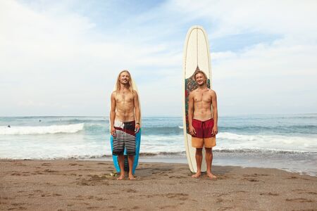 Surfing. Young Surfers Standing On Sunny Beach. Smiling Men Near Surfboards In Sand. Active Lifestyle, Water Sport On Beautiful Ocean Background.の写真素材