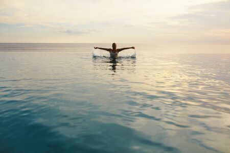 Ocean. Woman Standing In Sea. Girl Splashing Water Surface And Looking At Camera. Beautiful Seascape And Female Silhouette. Vacation In Tropical Country.の写真素材