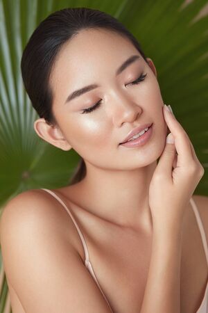 Beauty. Model Face On Palm Background. Asian Woman With Closed Eyes Enjoying Smooth, Hydrated And Glowing Skin. Organic Cosmetic And SPA Treatment For Perfect Body And Wellness.の写真素材