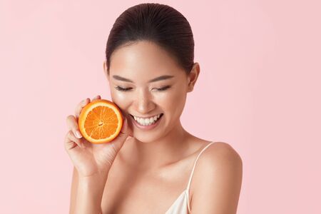 Beauty. Woman And Fruit Portrait. Happy Asian Model Holding Juicy Orange Near Face And Looking Down On Pink Background. Beautiful Ethnic Girl Uses Citrus And Natural Vitamins For Healthy Skin.の写真素材
