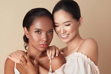 Beauty. Diversity Women Portrait. Different Ethnicity Models With Natural Makeup And Perfect Skin Against Beige Background. Happy Asian Girl Hugs Mixed Race Female Standing Together.の写真素材