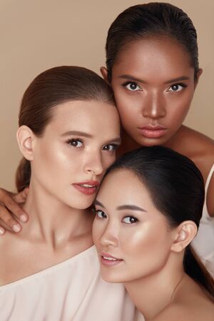 Beauty. Diverse Models Portrait. Tender Caucasian, Asian And Mixed Race Women Posing Together On Beige Background. Female With Perfect Skin And Natural Makeup Looking At Camera.の写真素材
