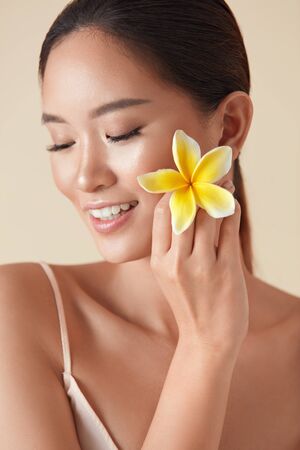 Woman. Beauty And Flower Portrait. Asian Model With Closed Eyes Holding Plumeria Near Face. Natural Treatment In SPA Salon For Healthy, Glowing Hydrated Facial Skin And  Perfect Body.の写真素材