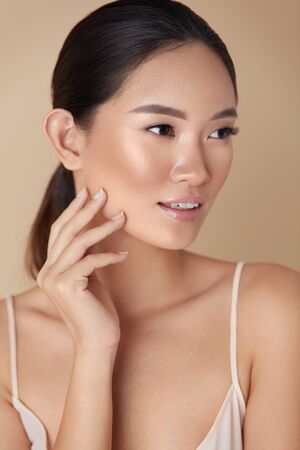 Skin Care For Perfect Look. Portrait Of Asian Model With Smooth Skin Touching Her Face And Looking Away. Female Enjoying Hydrated Skin After Daily Beauty Routine Or Cosmetology Treatment.の写真素材
