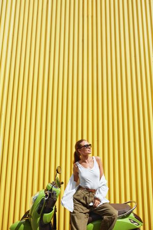 Urban. Fashion Girl On Moped Portrait. Sexy Model In Casual Clothes And Sunglasses Against Yellow Iron Fence. Beautiful Woman In White Shirt And Top Tank On Personal City Transport.の写真素材