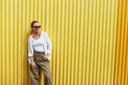Stylish Girl. Portrait Of Sexy Woman. Fashion Model In Casual Clothes And Sunglasses Standing Against Yellow Metal Fence. Female In White Shirt And Top Tank. Urban Lifestyle.の写真素材