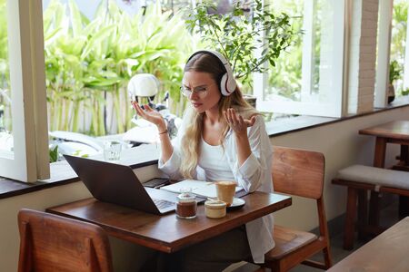 Work. Confused Woman At Coffee Shop. Beautiful Girl In Casual Clothes With Laptop And Headphones Having Online Meeting. Digital Technologies For Comfortable Life On Vacation And Successful Business.の写真素材