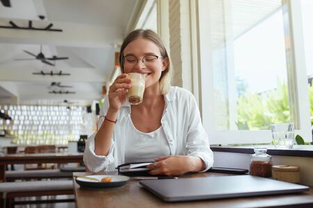 Business. Woman Drinks Coffee At Cafe. Happy Stylish Girl In Glasses With Laptop And Planner Book Enjoying Latte. Digital Technologies For Remote Work Or Online Studying At Comfortable Place.の写真素材