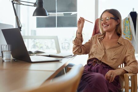 Entrepreneur. Fashion Designer At Workshop. Business Owner Working On Laptop And Creating Fashionable Dresses. Successful Self Employed Woman In Stylish Clothes Enjoying Her Job At Studio.の写真素材