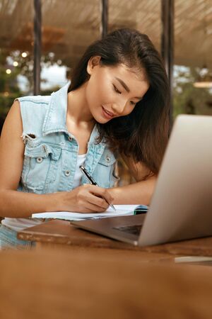 Woman. Working Online At Cafe. Asian Girl In Casual Clothes Using Laptop And Writing Something In Planner Book.の写真素材