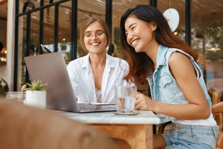 Women Chatting Online At Cafe. Girls In Casual Clothes Using Laptop For Video Meeting. Comfortable Digital Nomad Lifestyle With Modern Technologies For Communication.の写真素材
