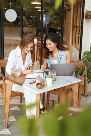 Women On Online Meeting At Cafe. Happy Girls In Casual Clothes Using Laptop On Terrace And Chatting With Somebody. Modern Technologies For Remote Job Or Education At Comfortable Workplace.の写真素材