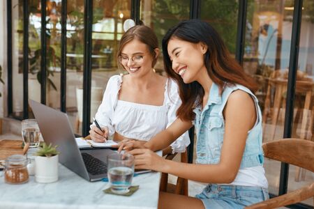 Girls Working At  Coffee Shop. Women With Laptop Having Meeting At Cafe. Beautiful Colleagues In Casual Clothes Using Modern Technologies For Communication And Supporting Business.の写真素材