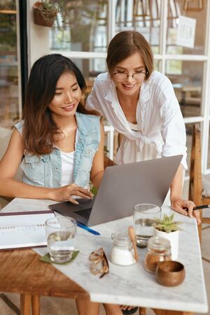 Women Working At Cafe. Girls In Casual Clothes Using Laptop And Having Discussion About Business. Modern Digital Nomad Lifestyle With Technologies For Creativity Online Job.の写真素材