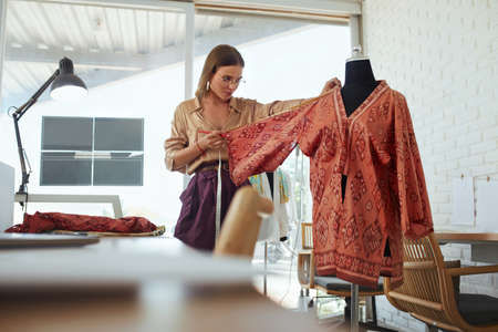 Workshop. Fashion Designer Working At Own Atelier. Beautiful Dressmaker In Elegant Clothes Measuring Dress On Mannequin. Happy Woman Tailor In Glasses Has Success Business.の写真素材