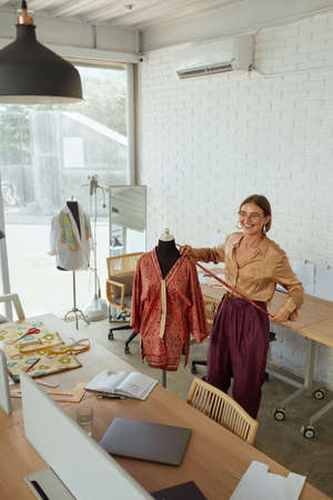 Workshop. Fashion Designer At Work. Professional Female Tailor Measuring Dress On Mannequin And Sketch Something. Successful Self Employed Woman Working At Own Clothing Atelier.の写真素材