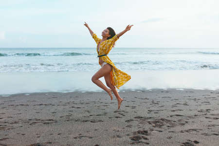 Summer. Girl On Beach Enjoying Vacation At Tropical Ocean. Stylish Model In Boho Dress With Floral Pattern Walking On Sandy Coastline And Feels Freedom. Bohemian Clothing Style For Fashion Look.の写真素材