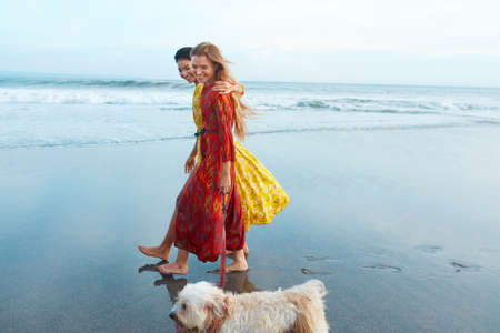 Dog-Friendly Beach. Women Walking With Pet On Sandy Coast And Enjoying Summer Vacation Near Ocean. Stylish Girls In Bohemian Dress Having Fun. Boho Clothing Style For Fashion Look On Resort.の写真素材
