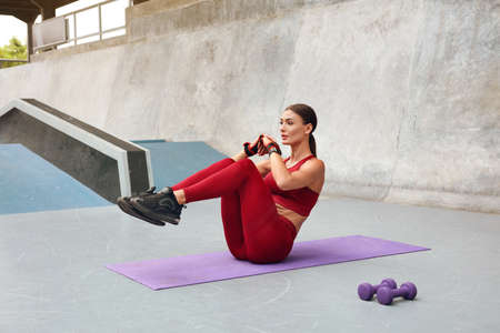 Fitness Girl Doing Leg Workout On Yoga Mat At Outdoor Stadium. Fit Woman With Strong Muscular Body In Fashion Sporty Outfit Doing Exercise Against Concrete Wall. Active Lifestyle For Urban People.の写真素材