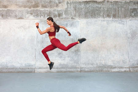 Fitness Girl Jumping. Outdoor Workout Against Concrete Wall At Stadium. Fashion Sporty Female With Strong Sexy Body In Dynamic Action Pose. Sport For Active Urban People.の写真素材