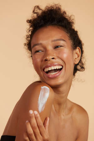Body skin care. Smiling black woman applying body cream portraitの写真素材
