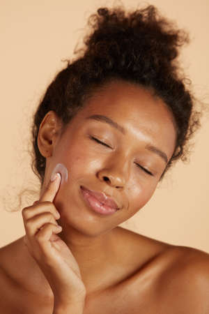 Face skin care. Woman applying cosmetic cream on skin portraitの写真素材