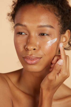 Face skin care. Woman applying cosmetic cream on skin portraitの写真素材