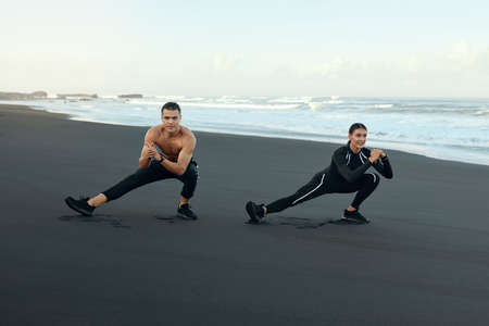 Sport Couple On Beach Stretching. Handsome Man And Sexy Woman In Fashion Sportswear Warming Up Before Training Outdoor. Workout On Sandy Coast As Lifestyle For Young Active People.の写真素材