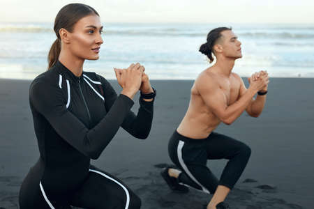 Sport Couple On Beach Squatting. Handsome Man And Sexy Woman In Fashion Sporty Outfit Training Outdoor. Young People Warming Up Before Workout On Sandy Coast. Active Vacation As Lifestyle.の写真素材
