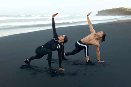 Beach. Man And Woman Warm Up Before Workout. Sport Couple In Fashion Sportswear Doing Stretching Exercise With Raising Hand. Outdoor Training On Vacation As Lifestyle For Active Peopleの写真素材