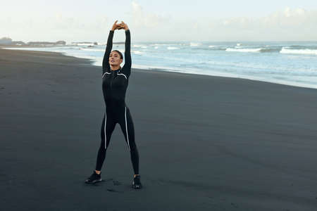 Beach. Fitness Girl Stretching On Coast. Sporty Woman With Perfect Body In Fashion Sportswear Warming Up Before Intense Workout Outdoor. Training On Resort At Sunrise As Part Of Active Lifestyle.の写真素材