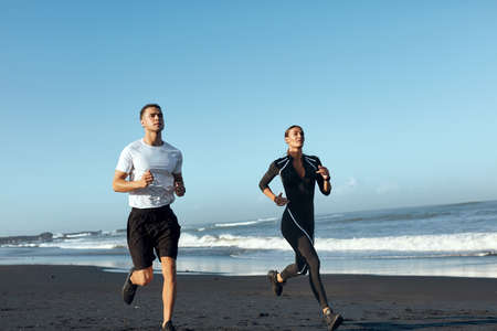 Beach. Woman And Man Running Along Coastline. Sport Couple In Fashion Sportswear On Outdoor Workout In Morning. Jogging Exercising Near Ocean On Summer Vacation As Part Of Active Lifestyle.の写真素材