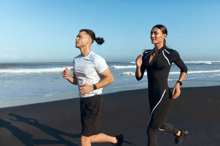 Couple Running On Beach. Handsome Man And Sexy Woman In Fashion Sporty Outfit Jogging Along Ocean Coast In Morning. Active Lifestyle And Recreation Sport On Summer Vacation.の写真素材