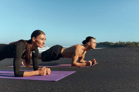 Beach. Couple Workout On Yoga Mat. Handsome Shirtless Man And Sexy Woman Doing Plank In Morning On Coast. Exercises For Strong Muscular Body On Summer Vacation.の写真素材