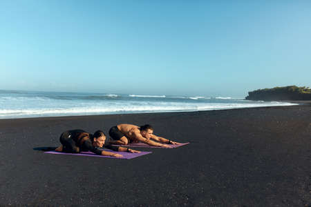 Couple Workout On Beach. Handsome Man And Sexy Woman In Fashion Sporty Outfit Stretching On Yoga Mat In Morning. Male And Female Doing Flexibility Exercise. Active Summer Vacation At Tropical Sea.の写真素材