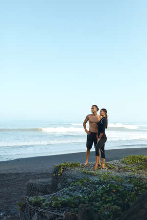 Beach. Woman And Man At Tropical Ocean. Sport Couple Resting After Workout And Looking Away. Full-Length Portrait Of Handsome Shirtless Guy And Sexy Girl In Fashion Sporty Outfit.の写真素材