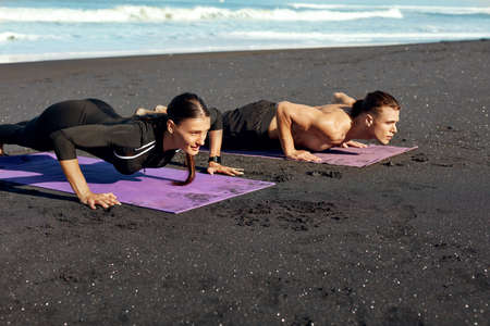 Couple Workout On Beach. Handsome Man And Sexy Woman In Fashion Sporty Outfit Doing Push-Ups On Yoga Mat In Morning. Active Lifestyle And Recreation Sport On Summer Vacation.の写真素材