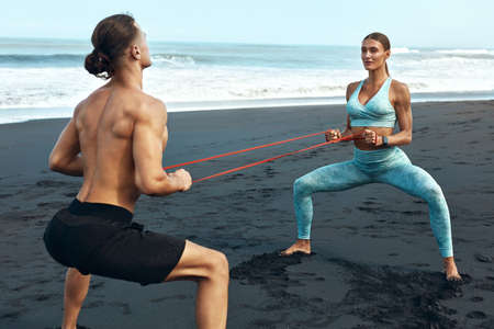 Sport. Couple On Beach Stretching With Resistance Band. Handsome Man And Sexy Woman In Fashion Sporty Outfit Training. Partner Workout Outdoor On Summer Vacation As Lifestyle.の写真素材