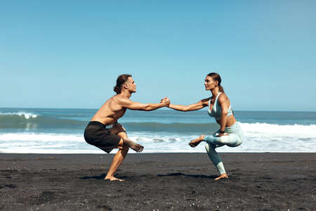 Fitness. Couple On Beach Doing Partner Squats. Shirtless Man And Sexy Woman In Fashion Sporty Outfit Workout On Coast. Male And Female Training Outdoor. Active Summer Vacation At Tropical Sea.の写真素材