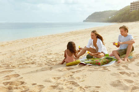 Summer. Family Picnic On Beach. Portrait Of Young Woman With Son Enjoying Lunch At Tropical Ocean. Mother And Handsome Boy On Vacation Near Sea. Organic Fruit And Natural Vitamins.の写真素材