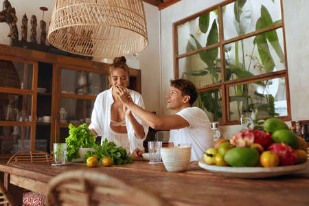 Lunch. Couple Cooking At Kitchen. Happy Man Feeding Beautiful Woman While She Preparing Fresh Organic Vegetables For Salad. Natural Vitamins For Nutrition As Part Of Healthy Lifestyle.の写真素材