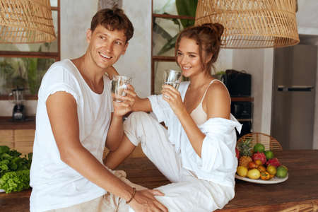 Couple Drinking Water At Kitchen. Romantic Man And Woman Holding Glasses And Looking Away. Detox Diet And Hydrate For Recovery As Part Of Healthy Lifestyle.の写真素材