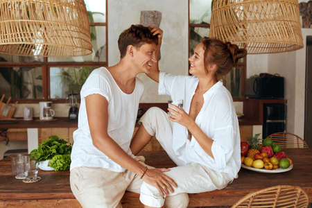 Healthy Diet. Couple Drinking Pure Water. Romantic Man Hugs Woman Touching His Hair And Holding Glass At Kitchen In Tropical Villa. Detox And Hydrate On Summer Vacation.の写真素材