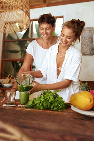 Healthy Diet. Couple Cooking Fresh Organic Food For Lunch. Romantic Man Hugs Woman Pouring Smoothie Into Glass At Kitchen In Tropical Villa. Natural Vitamins For Nutrition On Summer Vacation.の写真素材