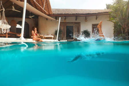 Man And Woman At Pool. Couple In Love Enjoying Summer Vacation At Tropical Villa. Male Diving In Water From Poolside, Beautiful Female Having Fun. Summertime At Resort For Positive Emotions.の写真素材