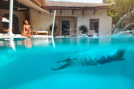 Summer. Couple Having Fun At Pool On Vacation. Man Diving Underwater And Splashing Turquoise Water. Beautiful Woman Looks At Snorkeler And Smiles. Honeymoon At Tropical Resort.の写真素材