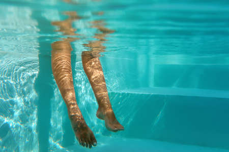 Underwater. Woman Keeping Legs In Pool While Sitting On Poolside. Female Enjoying Turquoise Water And Leisure At Resort. Recreation On Summer Vacation.の写真素材