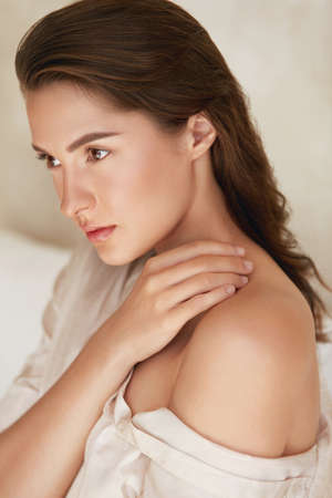 Beauty. Woman With Natural Makeup And Glowing Hydrated Facial Skin. Portrait Of Beautiful Model Touching Naked Shoulder And Looking Away.の写真素材