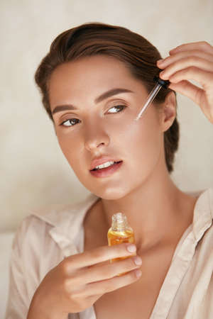 Beauty Face. Woman Applying Essential Oil On Facial Skin And Looking Away. Beautiful Model Moisturizing Derma With Natural Vitamin E, Serum Collagen And Hyaluronic Acid.の写真素材